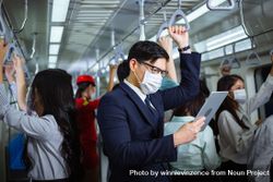 Businessman standing reading digital tablet in busy metro car bEv1M0