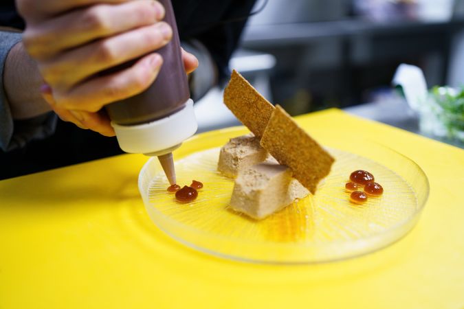 Hand squeezing sauce onto decorative appetizer