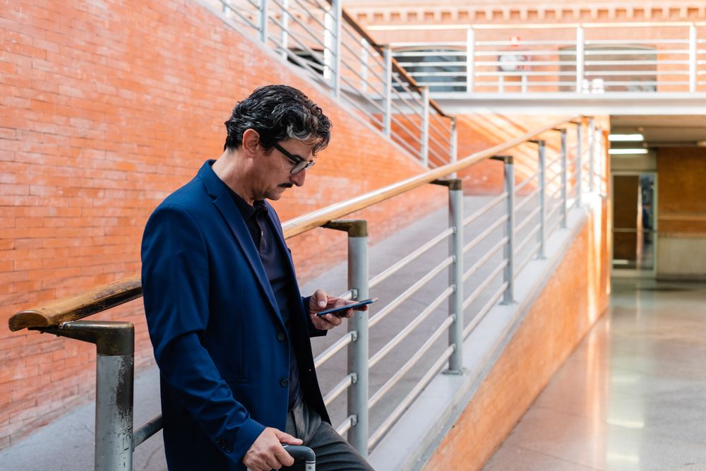 Mature man standing with baggage and talking on smartphone