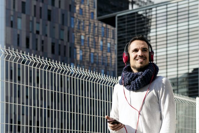 Smiling man listening to music on headphones while holding a mobile phone walking outdoor