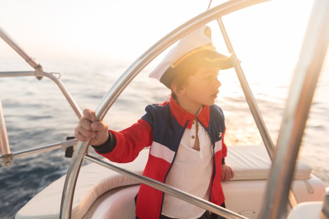 Smiling boy holding steering wheel on yacht on water