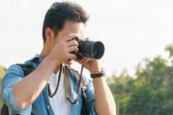 Man with camera to his face in a park with trees on overcast day