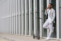 Elegant Black man talking smartphone leaning building