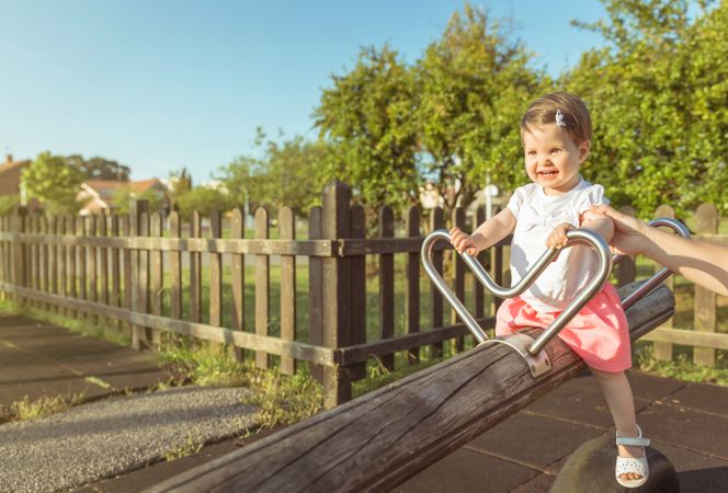 Baby girl playing over a seesaw swing on the park