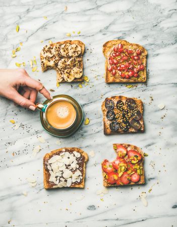 Toast topped with fresh fruit on marble background with hands holding coffee