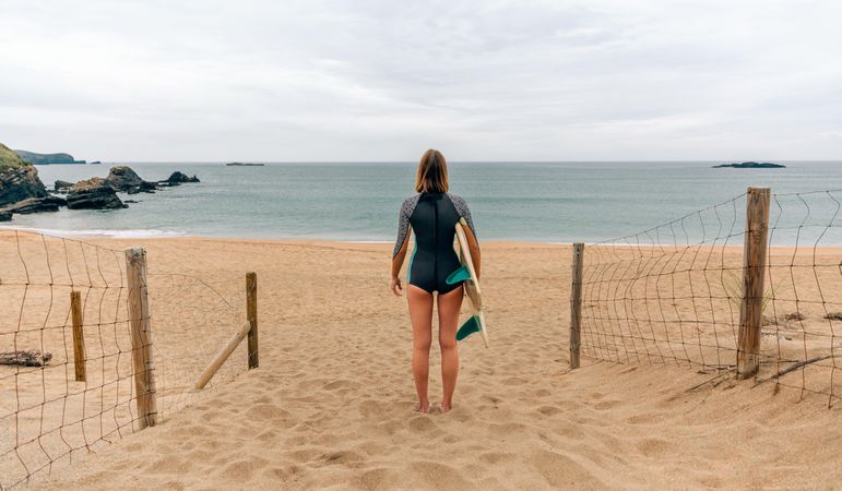 Woman standing on beach with surfboard enjoying beautiful view