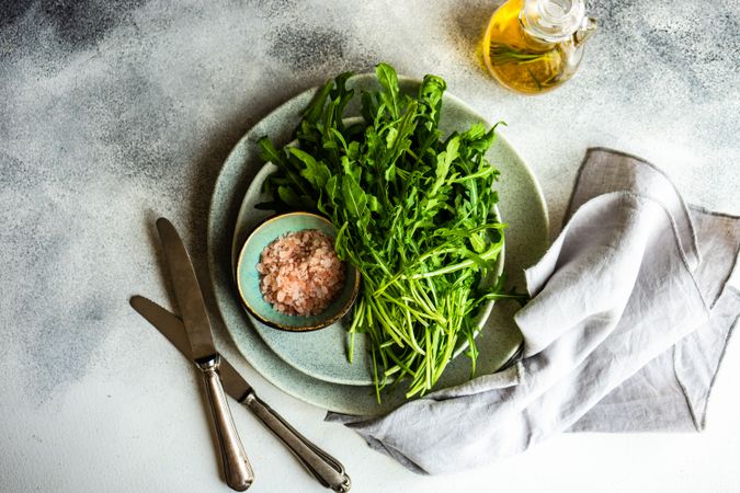 Looking down at plate with bunch of arugula and pink salt served with olive oil