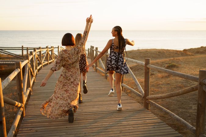 Back of three woman walking on pedestrian walkway towards beach