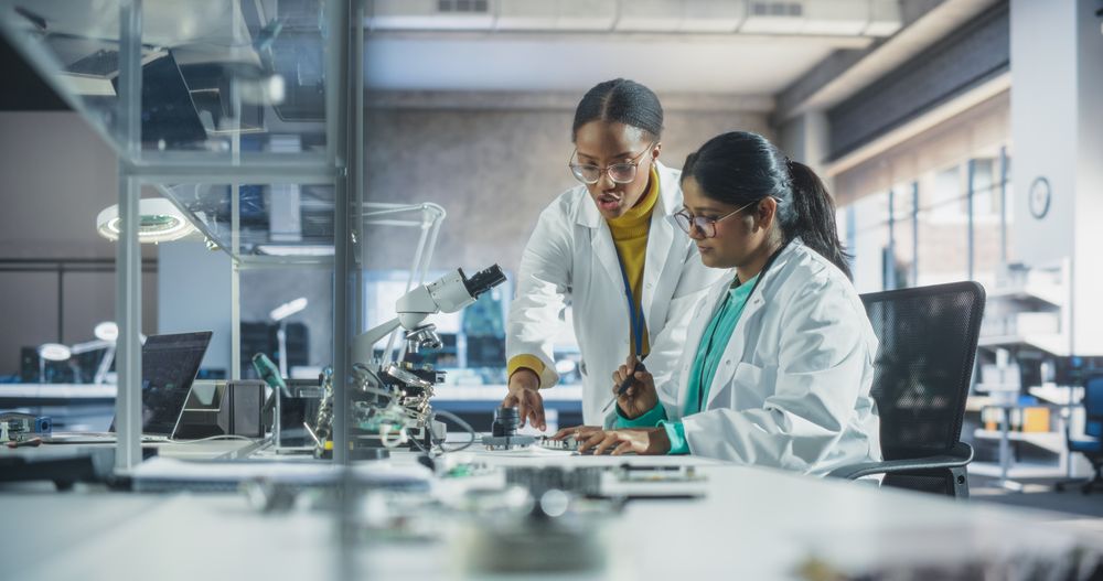 Indian Woman Having a Conversation with a Mentor in a Laboratory, While Working on a Circuit Board for a Project.