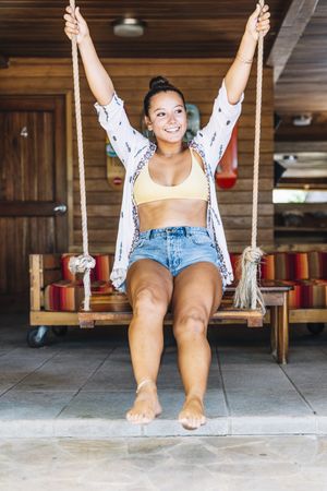 Cheerful woman riding on swings on tropical terrace