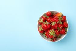 Bowl with tasty strawberry on blue background. Summer berry