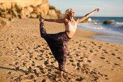 Blonde female doing leg stretches facing the ocean on beach