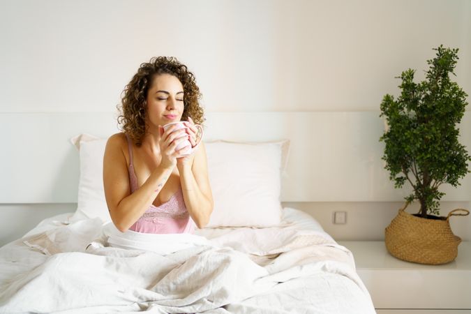 Relaxed woman holding fresh aromatic coffee in bed at home