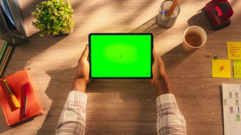 Creative Black Person Holding a Tablet, Viewing Content on a Computer with Green Screen Mock-Up Display. Photo Template with Placeholder for Small Business Advertising and Corporate Content