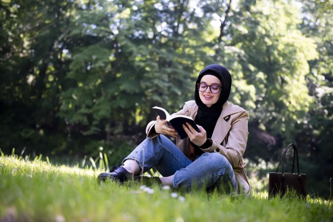 Relaxed Middle Eastern woman with book sitting on the grass