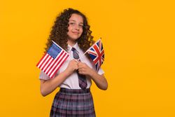 Girl with slight smile holding USA and UK flags.