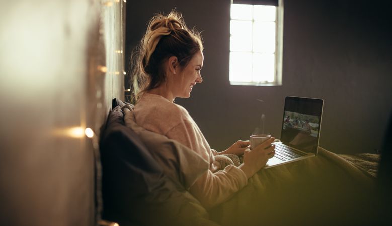 Woman on bed using laptop and having coffee.
