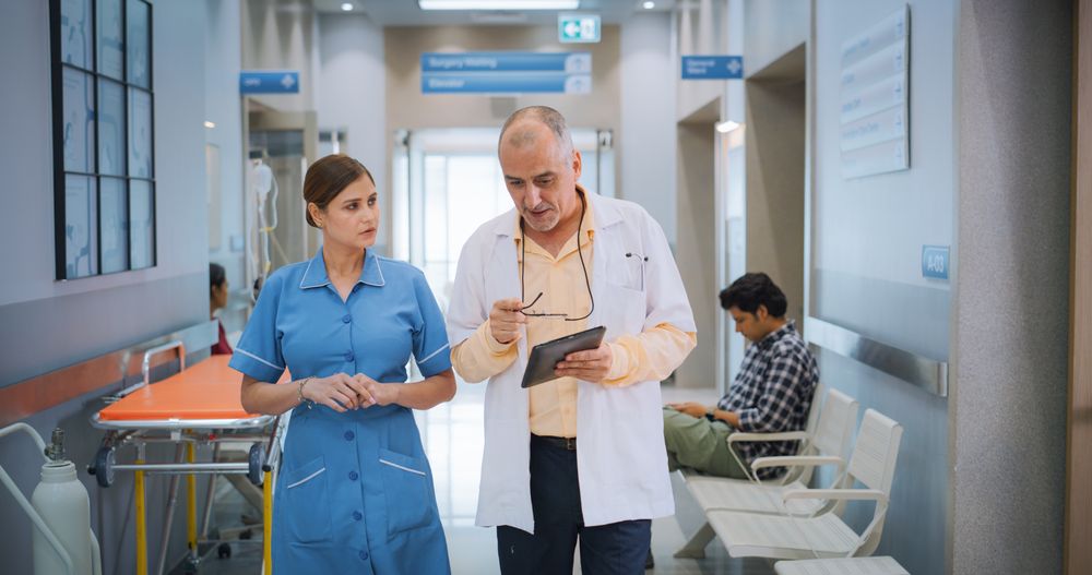 Portrait of Indian Male Doctor and Female Nurse Walking in Hospital Corridor and Talking while Using a Digital Tablet.