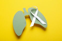 Green lungs cut out of paper with ribbon on yellow background