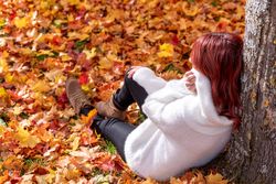 Woman leaning on tree trunk in park in autumn