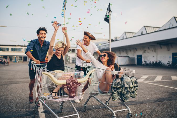 Two couples having fun in shopping carts throwing confetti