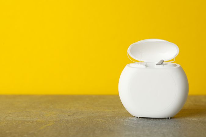 Tooth floss on gray table against yellow background, space for text