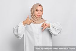 Asian female in headscarf with with hands making alternate thumb gesture 5az2a4