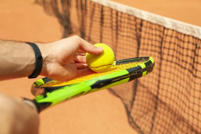 Man hold racket with tennis ball against clay court