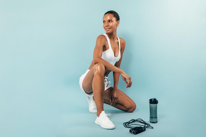 Smiling woman sitting in blue studio after working out with jump rope and water bottle