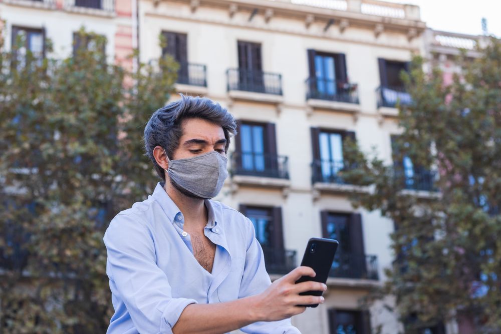 Man in mask browsing smartphone on street