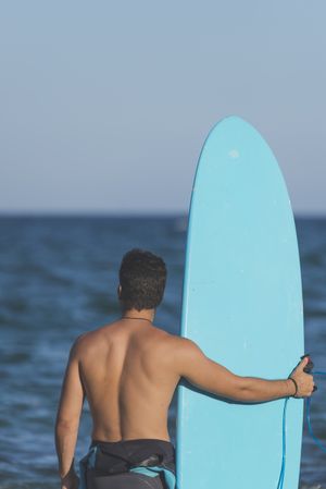 Male surfer with blue board standing in front of the sea