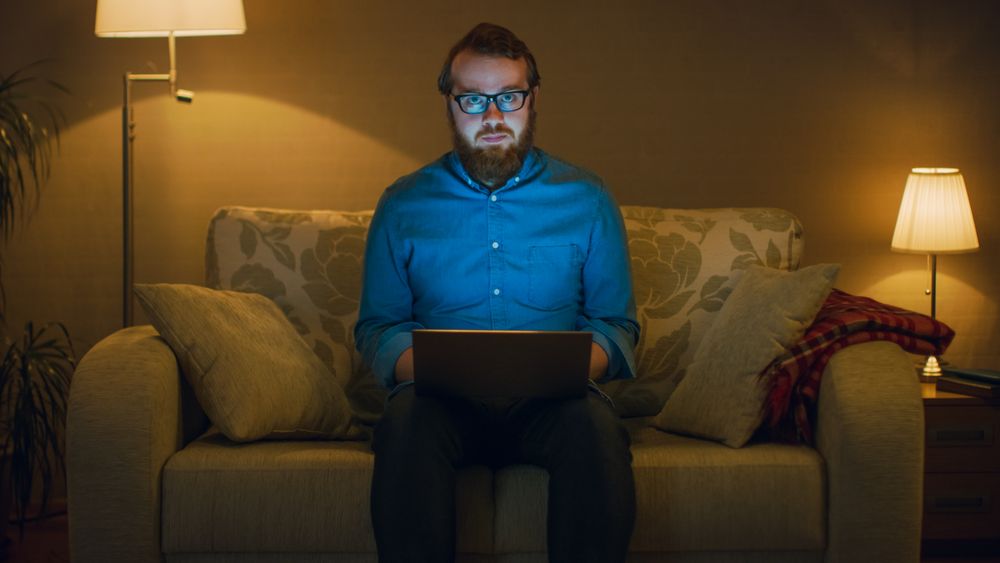 Portrait Shot of a Man Sitting on a Couch in His Living Room, Laptop on His Knees.