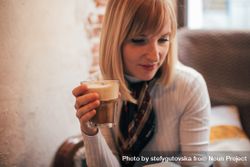 Blonde woman holding latte drink in cafe 0PPal0