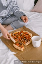 Cropped image of a person in a pajama eating pizza on bed 5pKov0