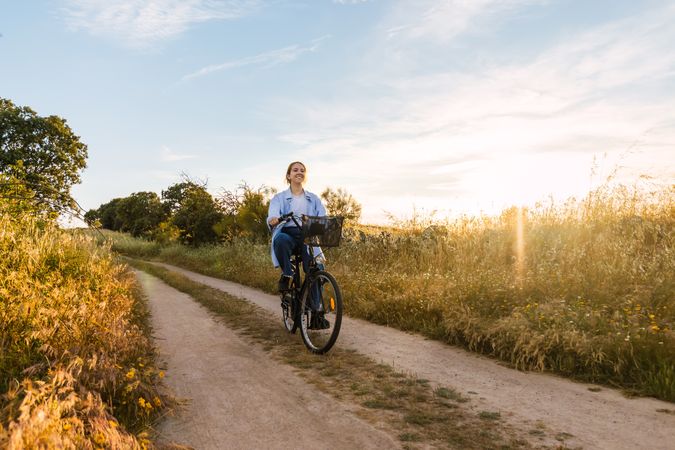 young blonde woman cycling in a field at sunset