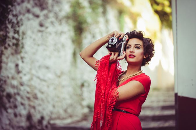 Elegant woman in dress and pearls taking a photo, copy space