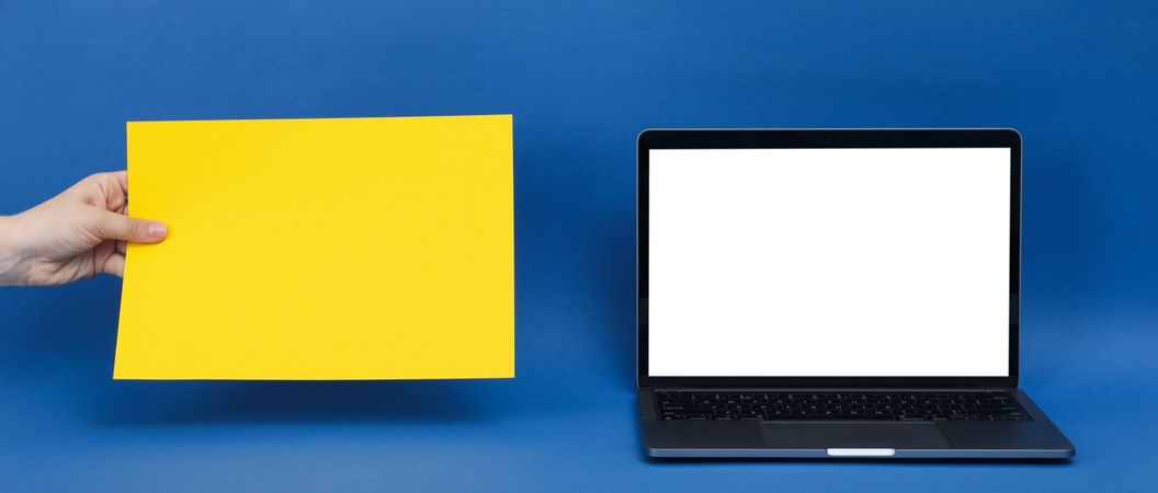 Mockup laptop screen with hands holding yellow paper next to it for copy space