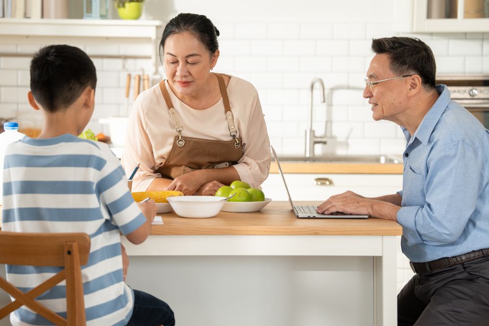Asian grandmother watching and talking with grandson while doing homework