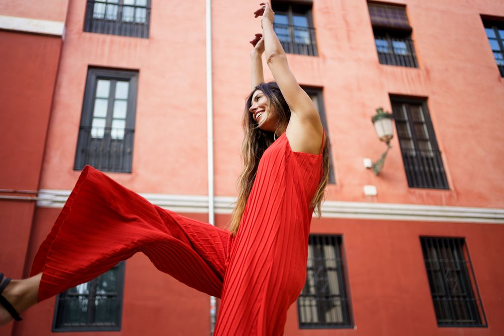 A Joyful Woman is Dancing Outdoors While Wearing a Red Dress in a Beautiful Setting