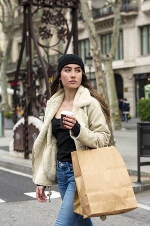 Portrait of young woman walking in a city street, with takeaway coffee and shopping bag