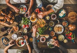 Group of people serving themselves tea and food at Turkish breakfast with eggs, breads, vegetables