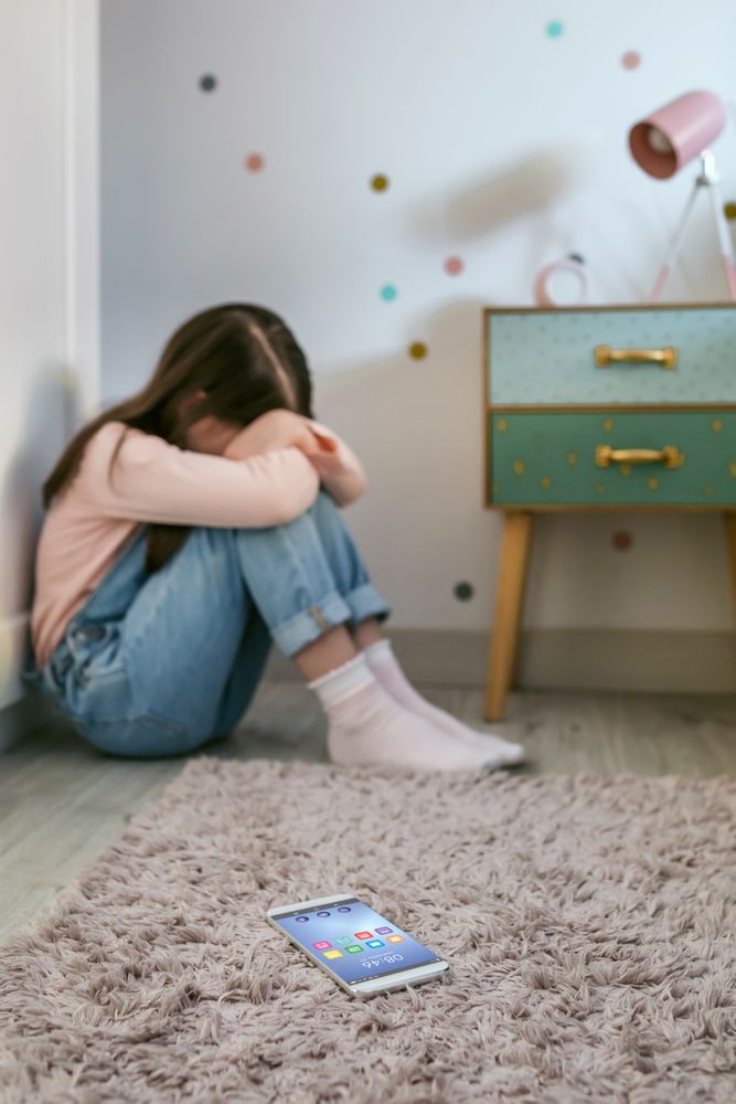 Cell phone lying on the floor with sad little girl crying sitting behind
