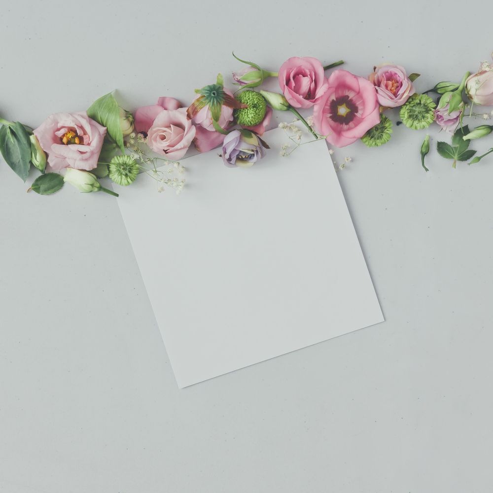 Line of pink flowers and leaves on marble background with paper card