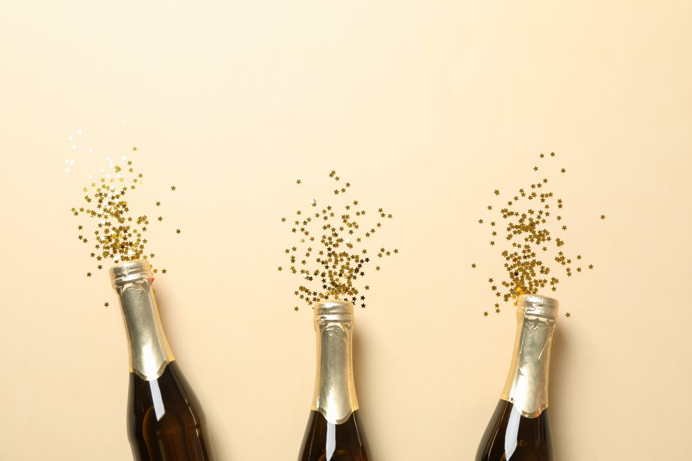 Champagne bottles and glitter on beige background, space for text