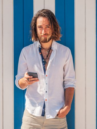 Smiling man browsing smartphone against striped wall