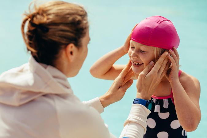 Teacher helping young girl put on swim cap