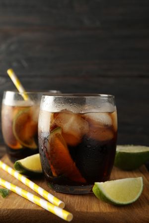Glasses with ice cola, lime slices and tubules on wooden background
