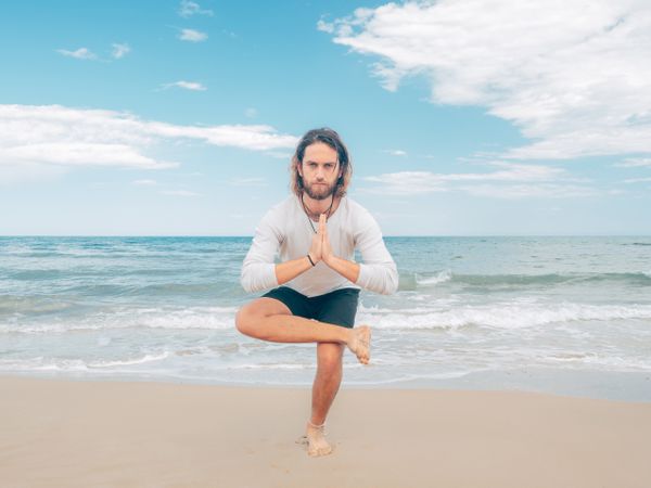 Man training yoga on beach