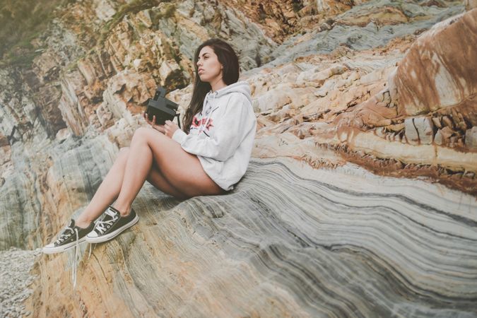 Woman with camera on shore near stones and water