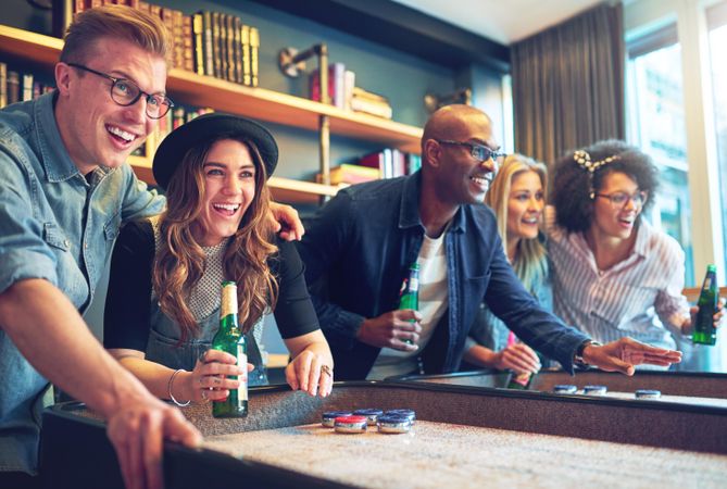 Multi-ethnic group of friends playing shuffleboard with beer in hand